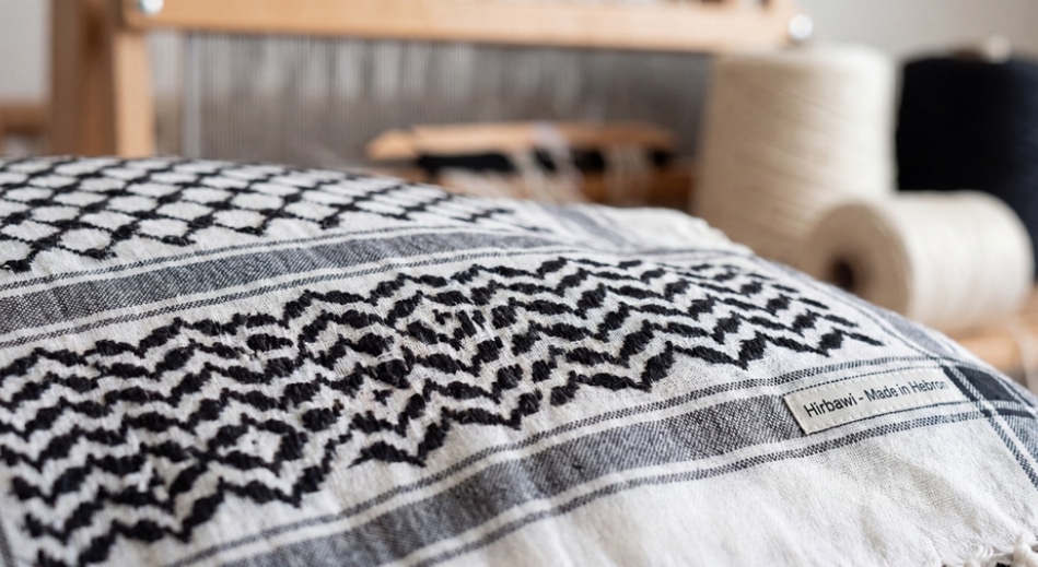 Keffiyeh Hirbawi Artisanal de Hébron en Palestine Keffiyeh Hirbawi noir et blanc avec étiquette 'Made in Hebron' sur un métier à tisser traditionnel.